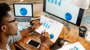 Data Analytics Specialist reviewing charts. Graphs on screen, data analysis in progress.
