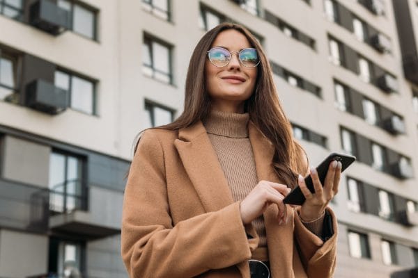 Adult matric English home language banner: Woman with phone, wearing coat and glasses.