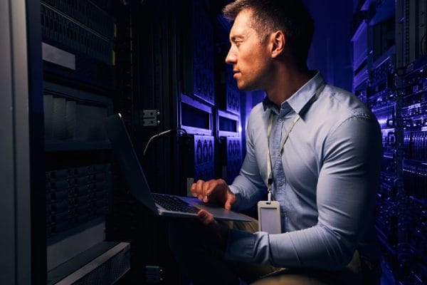 Apprentice developer working on servers. IT specialist with laptop in data center. Journeyman developer career.
