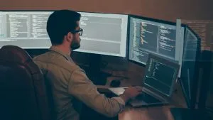 Programmer working on API development. Developer coding on multiple monitors.