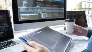 Software Project Analyst to Manager: Coder with laptop, coffee, and code on screen.