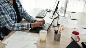 Technical bundle. Person working on a laptop. CompTIA course. Desk with computer, tablet, and paperwork.