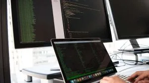 ISTQB CTFL: Software tester coding on laptop with dual monitors. Software testing, ISTQB certification.