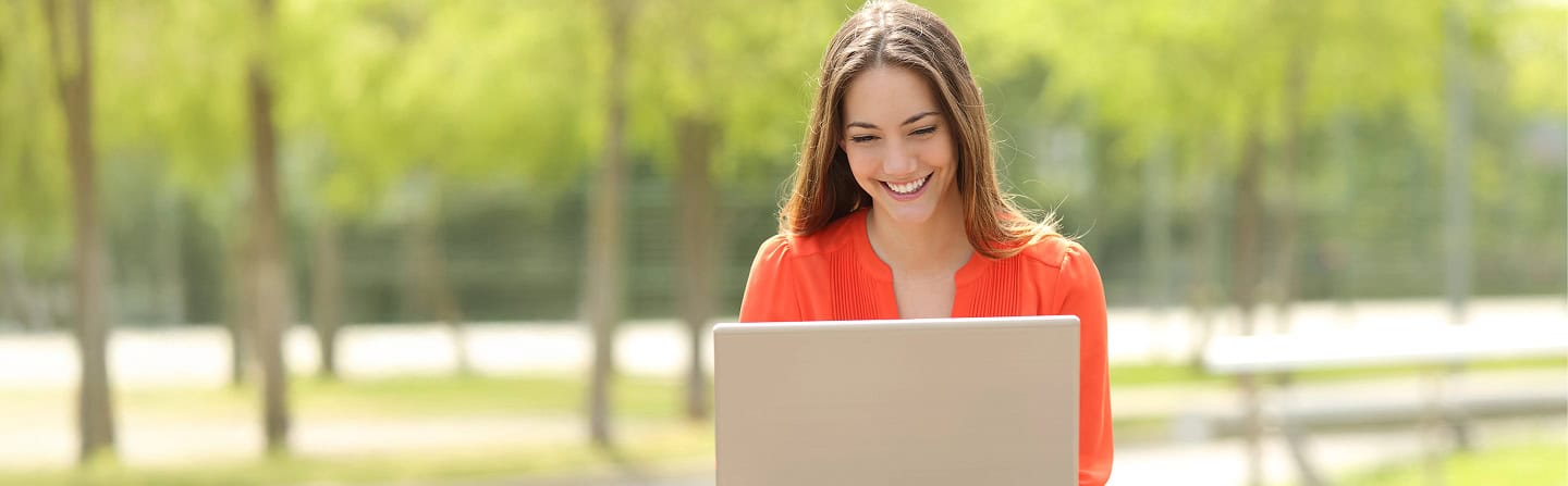 Student finance options: Smiling student using a laptop outdoors.